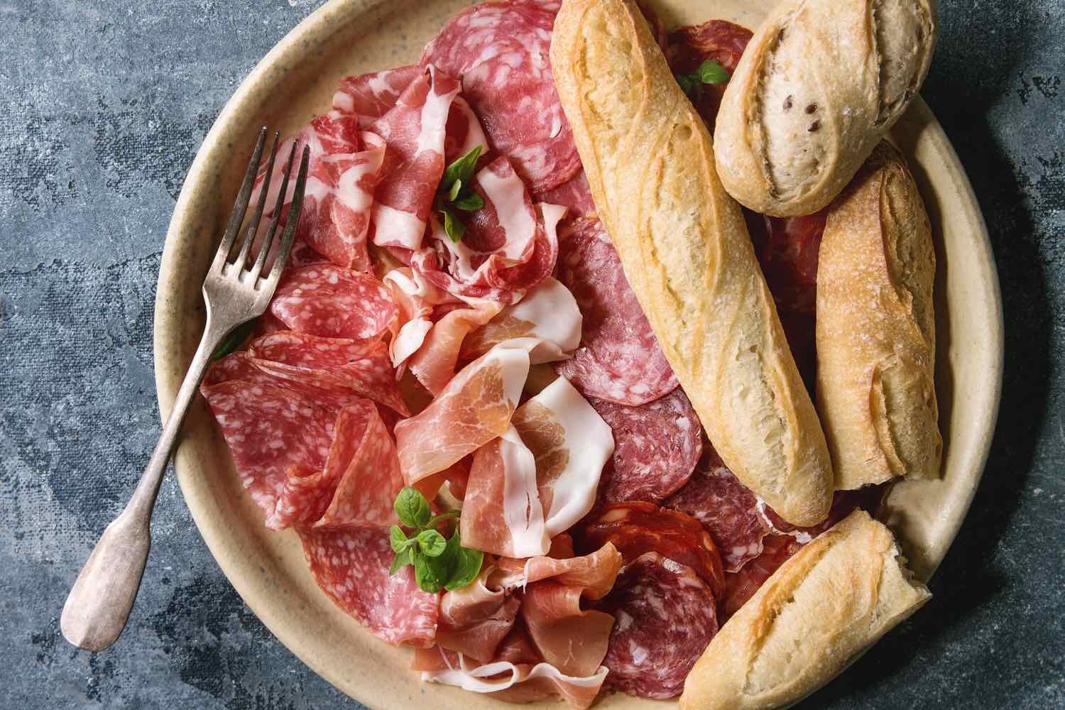 Antipasto meat platter assorti of sliced jamon, salami, chorizo sausage in ceramic plate with bread over blue texture background. Flat lay, close up