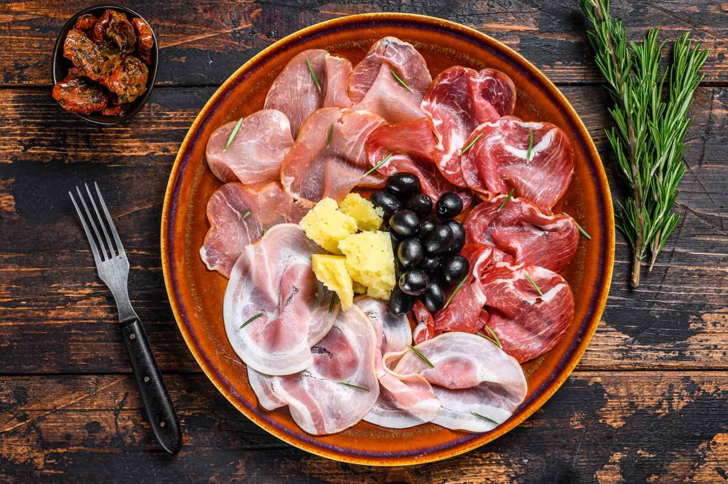 Italian meat platter with prosciutto ham, bresaola, pancetta, salami and parmesan. Dark wooden background. Top view.