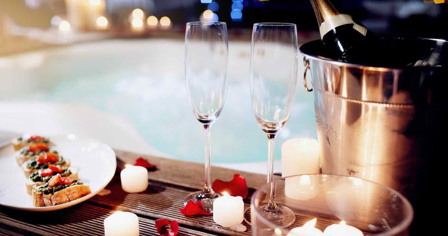 Shot of a beautiful setting of champagne and treats near a hot tub at night.