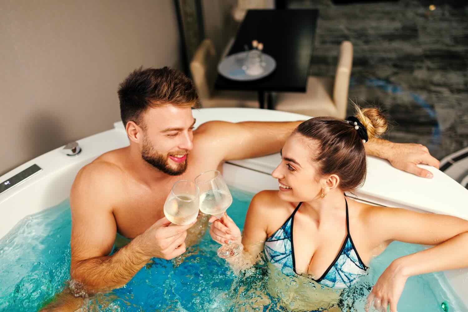 Young happy couple drinks wine and enjoys hot tub