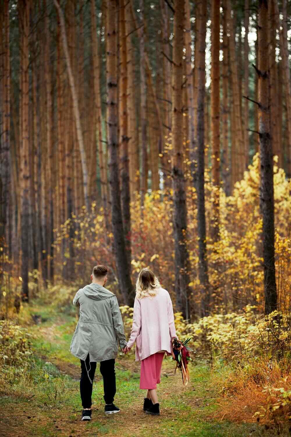 Couple in love walks through autumn forest. Hugs and kisses of men and women, relationships and love. Young couple stands in yellow red grass, a bouquet of flowers in girl hand